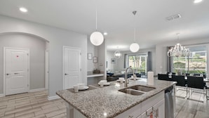 A modern kitchen with granite countertops, a double sink, and pendant lighting. - Disney Escape: Private Pool and Spa, Near Disney World ! (Kissimmee)
