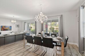 A modern kitchen with a dining area, large windows, and a chandelier. - Resort Access: 6BR Home w Pool near Disney (Kissimmee)