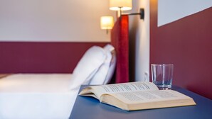 A hotel room with a bed, a bedside table with an open book and a glass of water, and a wall-mounted lamp. - Eclectic Apartment 1 in Vasto by Wonderful Italy (Napoli)