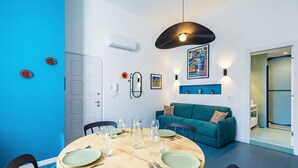 A dining area with a round wooden table set for four, surrounded by black chairs. A teal sofa is positioned against the wall, and a colorful abstract painting is displayed above it. - Eclectic Apartment 1 in Vasto by Wonderful Italy (Napoli)
