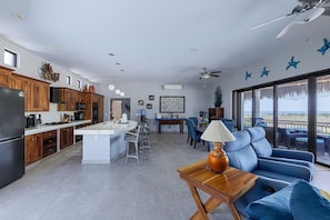 A modern kitchen with a central island, dining area with blue chairs, and a seating area with a sofa and table. - Sunny Poolside Escape Near the Beach (Los Barriles)