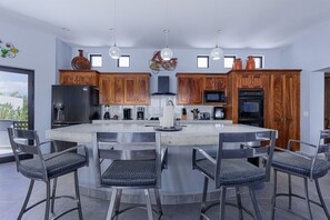 A modern kitchen with a central island, bar stools, and a dining area.