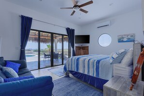 Ein Schlafzimmer mit Bett, einer Couch, einem Fernseher, einem Deckenventilator und Blick ins Freie.