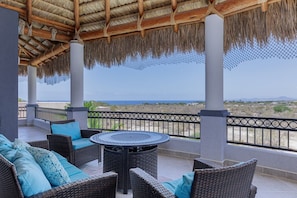 A covered outdoor seating area with wicker furniture and a table, overlooking a beach and ocean. - Sunny Poolside Escape Near the Beach (Los Barriles)