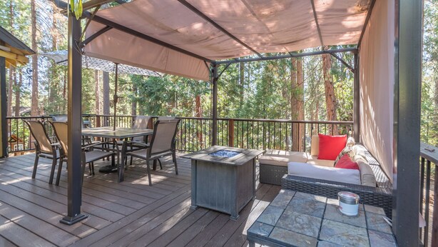 A covered outdoor deck with a table and chairs, a fire pit, and a seating area with cushions. - Greene Gables- Cozy Mountain Retreat (Avery)