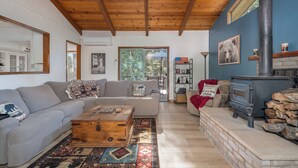 A cozy living room with a wooden ceiling, a sofa set, a coffee table, a fireplace, and a bookshelf. - Greene Gables- Cozy Mountain Retreat (Avery)