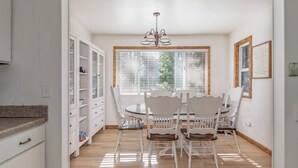 A bright kitchen with white cabinets, a dining table with white chairs, and a chandelier. - Greene Gables- Cozy Mountain Retreat (Avery)