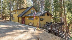 A yellow building with a red door, a flag, and a staircase leading to a deck. - Greene Gables- Cozy Mountain Retreat (Avery)