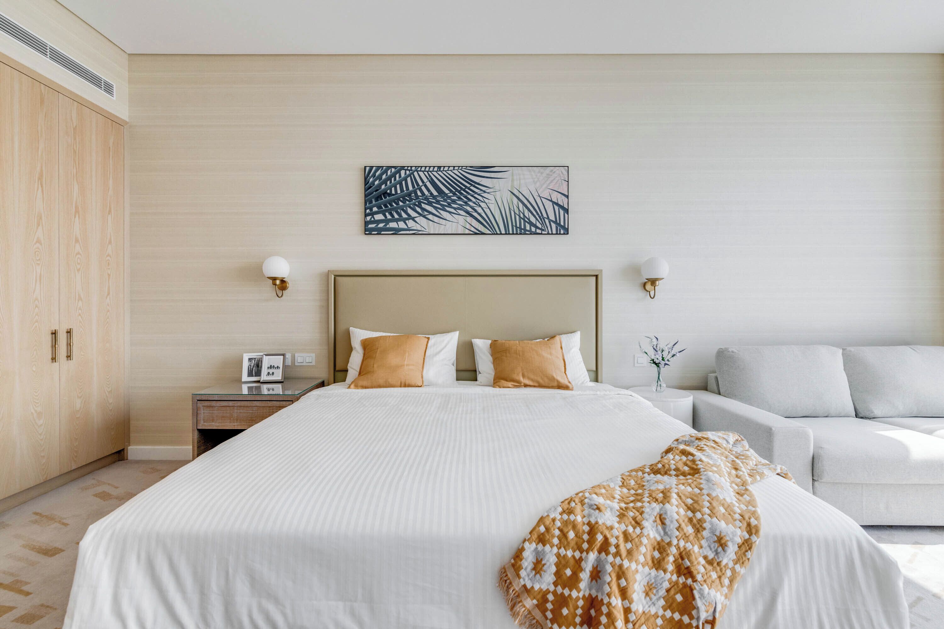 A hotel room with a large bed, a wooden wardrobe, a nightstand with a lamp, and a wall-mounted artwork.