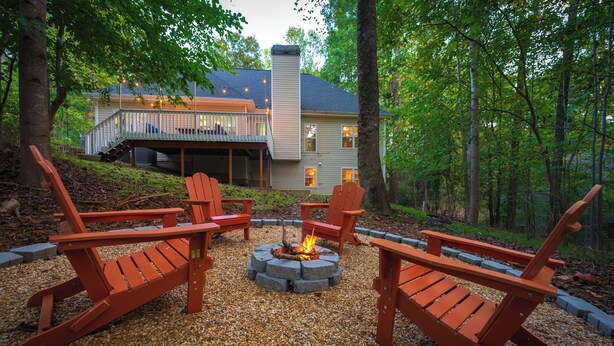 Una terraza con sillas Adirondack, un pozo de fuego y una casa al fondo.