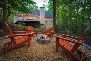 A deck with Adirondack chairs, a fire pit, and a house in the background. - Lake Lanier Retreat, Dock, Firepit, Home Theater,HotTub (Gainesville)
