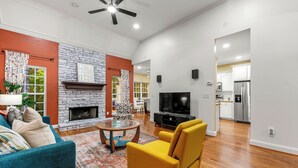 Un salón amplio con chimenea, televisor y zona de cocina al fondo.