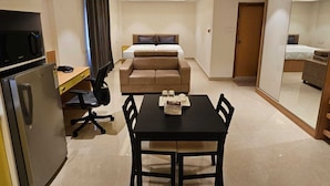 A compact hotel room with a bed, a desk with a computer, a microwave, a refrigerator, and a dining table with chairs. - Western Suites (Hyderabad)