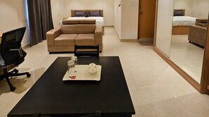 A hotel room with a bed, a sofa, a desk with a tray of items, and a mirror. - Western Suites (Hyderabad)