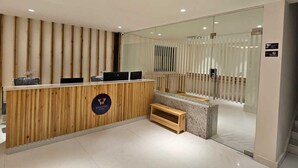 A reception area with a wooden reception desk, a seating bench, and a glass partition. - Western Suites (Hyderabad)