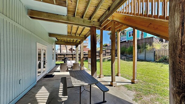 A covered patio area with a concrete floor, a picnic table, and a wooden pergola structure.