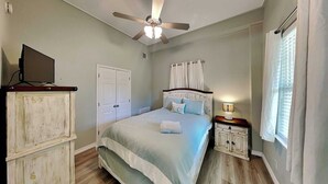 A bedroom with a bed, a ceiling fan, a nightstand, a TV, and a wardrobe.