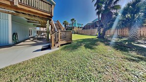 A two-story house with a wooden deck, a covered patio, and a fenced backyard with palm trees.