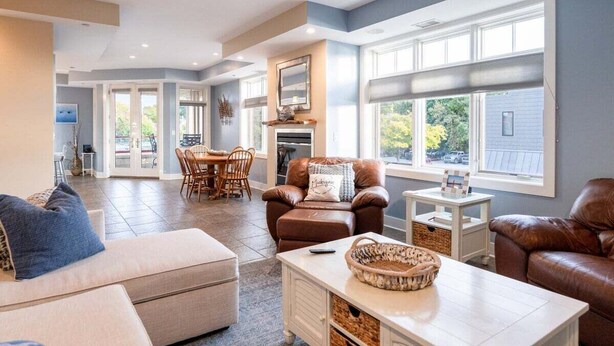 A spacious living room with a fireplace, leather sofas, and a dining area with a table and chairs. - Stunning Downtown Condo w/ Water Views (Grand Haven)