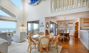 A spacious living area with a large dining table, comfortable seating, and a view of the ocean.