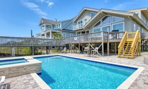 A two-story house with a swimming pool, outdoor furniture, and a wooden deck.