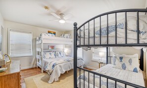 A bunk bed room with a ceiling fan, a desk with a chair, and a window with blinds.