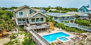 A beachfront property with a swimming pool, multiple decks, and a view of the ocean.