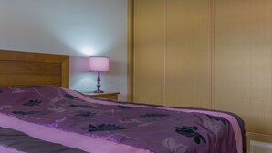 Quarto com cama, cabeceira de madeira, mesa de cabeceira com abajur e guarda-roupa de madeira.