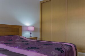 A bedroom with a bed, a wooden headboard, a nightstand with a lamp, and a wooden wardrobe. - Areca Apartment, Armação de Pêra, Algarve (Armação de Pêra)