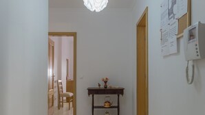 Um corredor com uma mesa de madeira, uma cadeira e um telefone fixado na parede.