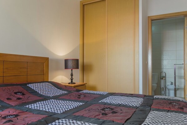 A bedroom with a wooden headboard, a quilt with floral patterns, a bedside lamp, and a closet with a sliding door.