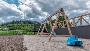 A playground with a swing set and a slide, surrounded by a fence and trees. - Cottage in Duszniki Zdrój with Spa Access (Duszniki Zdrój)