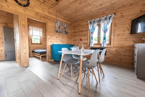 A wooden cabin interior with a dining table, chairs, a sofa, and a television.