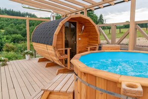 Un bain à remous en bois avec une piscine à l’eau cristalline, entouré d’une terrasse en bois et d’un espace salon couvert.