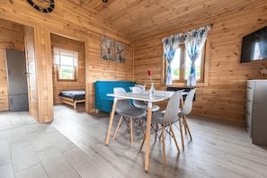A wooden cabin interior with a dining table, chairs, a sofa, a small bed, and a kitchen area.