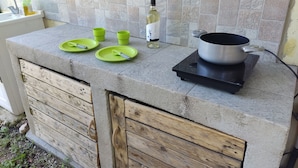A kitchen counter with a portable stove, green plates, and a bottle of olive oil. - Guesthouse Pintadera (Sassari)