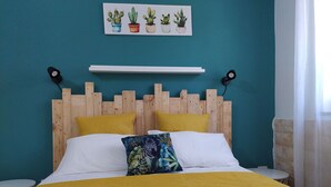 A bed with a wooden headboard, two yellow pillows, a colorful pillow, and a yellow bedspread. There are folded towels on the bed. - Guesthouse Pintadera (Sassari)