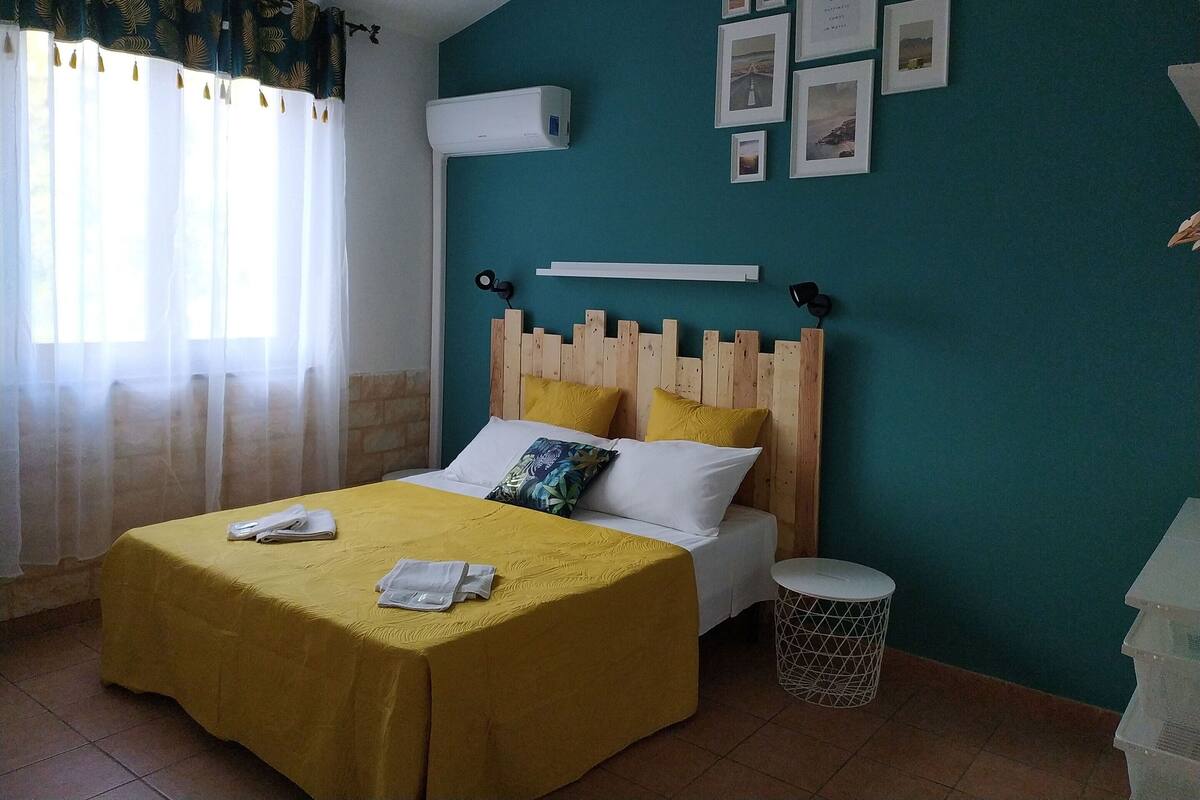 Un dormitori amb llit, una taula de nit, aire condicionat fixat a la paret i una finestra amb cortines.