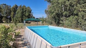 A rectangular swimming pool with a green canopy, surrounded by lush greenery and trees. - Guesthouse Pintadera (Sassari)