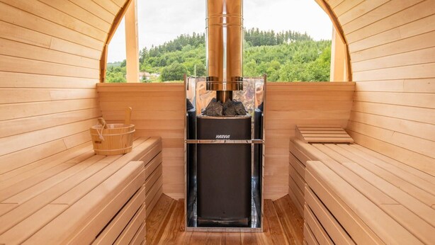 Una sauna con bancos de madera y vista a un bosque a través de un ventanal en arco.