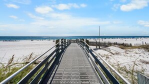 Een houten looppad dat naar een strand leidt, onder een heldere lucht.