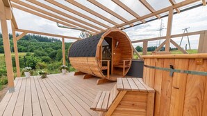 A wooden barrel-shaped structure with a staircase leading to a door, situated on a wooden deck with a view of a forested area. - Cottage in Duszniki Zdrój with Panoramic View (Duszniki Zdrój)