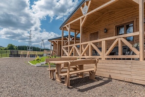 A wooden building with a covered patio area, outdoor seating, and a view of the surrounding landscape. - Cottage in Duszniki Zdrój with Hilltop Views (Duszniki Zdrój)