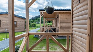 A wooden cabin with a balcony, a hanging planter, and a view of a green landscape.