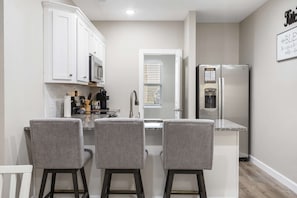 A kitchen with white cabinets, a stainless steel refrigerator, and a window with blinds. - Branson’s Like Home Hideaway (Branson)