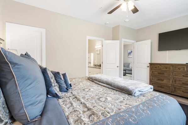 A bedroom with a large bed, a ceiling fan, a TV, and a dresser.