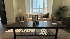 A living room with a dark wooden coffee table, a beige sofa, a lamp, and a potted plant.