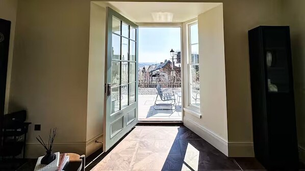 Une pièce avec une grande porte ouverte donnant sur un balcon d’où l’on peut admirer des immeubles et une rue.