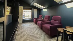 A room with a herringbone floor, a large window, and a row of red chairs.