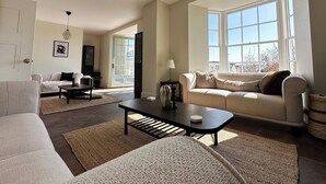 A spacious living room with a large window, a sofa, a coffee table, and a lamp.